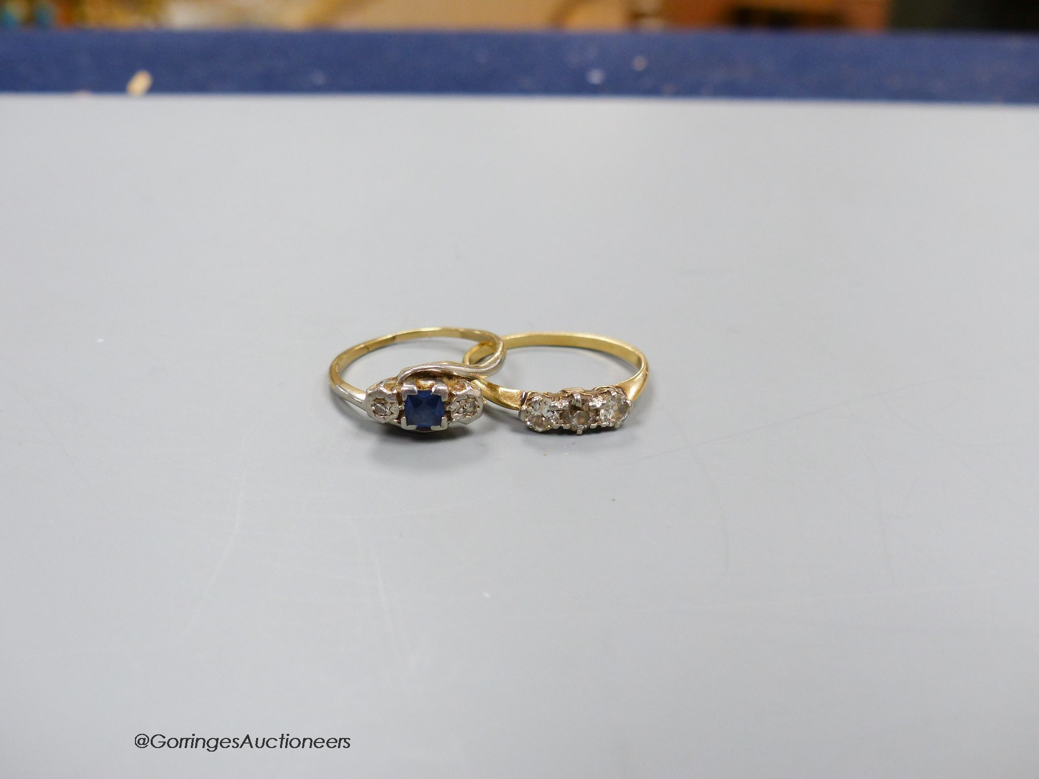A three stone diamond ring, size M, 2.4g, and a three stone diamond and sapphire ring, size O, 2.5g.